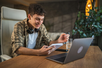 young man with headphones write notes in notebook watch video course