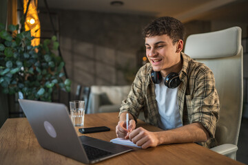 young man with headphones write notes in notebook watch video course