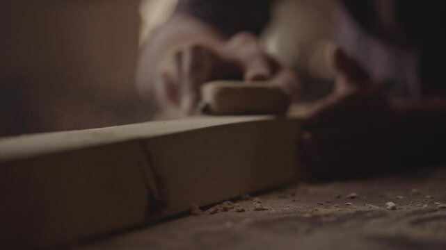 Close-up of a worker man using sandpaper to rub timber wood at workshop table in carpenter wood factory. Slow-motion footage