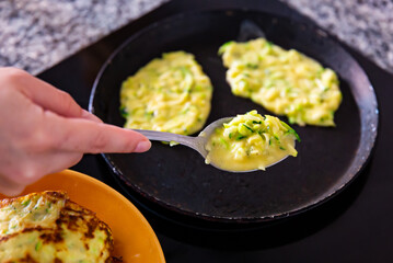 Appetizing zucchini pancakes fried in frying pan in kitchen