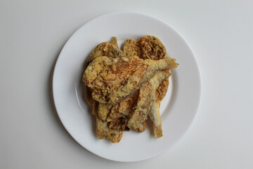 Fried fish. Preserved fish by salting method, half cut, flour coated, called Gereh or Ikan Asin in Indonesia. Isolated on white background, on white plate, flat lay or top view