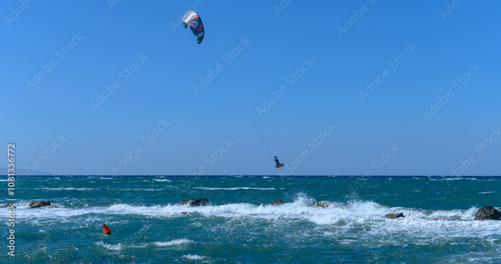 Wall mural Kite surfer soaring above waves on a bright sunny day at the coast