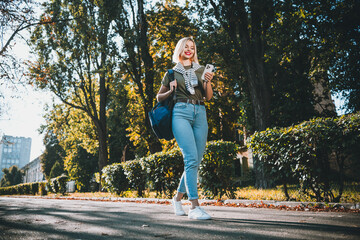 Full size photo of positive young blonde girl wear khaki outfit tied shoulders sweater walk hold...