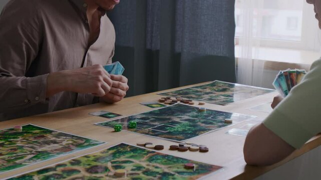 Midsection shot of man holding game cards and moving token on illustrated map while playing tabletop game with female friend at table in living room