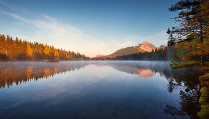 Fototapeta premium Peaceful Lake at Sunrise, With Mist Rising From the Water and a Lone Mountain Reflecting on the Calm Surface, Surrounded by Autumn Forests in Soft Morning Light