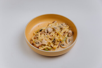 Creamy tagliatelle pasta with mushrooms and chicken in a beige bowl on a light background