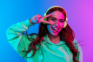 Photo of charming positive woman wear green sweatshirt headphones stick out showing v-sign isolated...