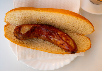 In fast food restaurant, appetizer of fresh baguette with juicy pork homemade sausage with cup of tea. Whole sausage lies between thick slices of bread, baguette, and smells fragrant of toasted meat