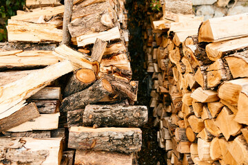 Rustic firewood stack in front of traditional house with stone wall backdrop