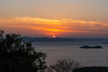 Stunning sunset over calm sea with the silhouette of an island and trees in the foreground - tranquil coastal landscape at golden hour.