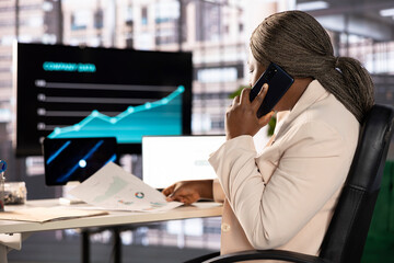 Businesswoman in telephone call with shareholders, analyzing market trends and data in office. Entrepreneur talking on phone with partners to develop trading strategies and algorithms