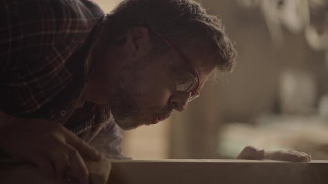 Young carpenter polishing wooden craft at workbench in woodworking workshop. Slow-motion footage