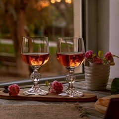 Two wineglasses of pink wine. Square. Atmospheric mood, beautiful reflections in glasses of wine. Pink Wine. Miniature roses