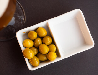 Bowl of green pickled olives with stone. On table there is ceramic bowl with vegetable snack for beer, wine
