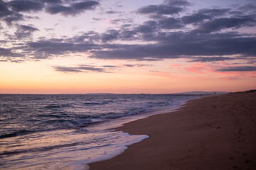 Obraz premium A serene beach at sunset with gentle waves lapping the shore and a colorful sky transitioning from orange to purple hues