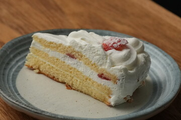 One small Japanese strawberry shortcake on a stylish Japanese plate on a wooden tray on a black cloth on a white table