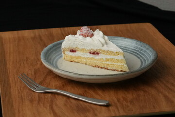 One small Japanese strawberry shortcake and a small fork on a stylish Japanese plate on a wooden tray on a black cloth on a white table