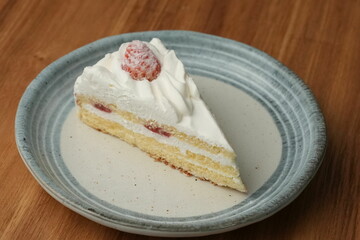 One small Japanese strawberry shortcake on a stylish Japanese plate on a wooden tray on a black cloth on a white table