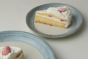 Two Japanese strawberry shortcakes, one on a stylish small plate and one on a large plate, on a white table