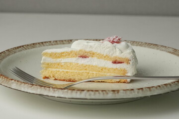 One small Japanese strawberry shortcake and a big fork on a stylish big plate on a white table