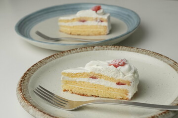 Japanese strawberry shortcake and fork on each stylish large and small plate on a white table