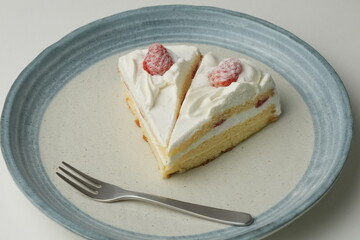 Two Japanese strawberry shortcakes and a large fork on a stylish large plate on a white table