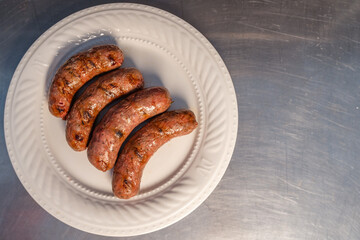 Grilled sausages presenting on a white plate over metal table