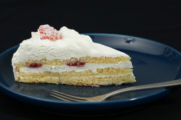 One small Japanese strawberry shortcake on a stylish Japanese plate and fork on a black cloth on a white table