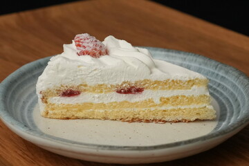 One small Japanese strawberry shortcake on a stylish Japanese plate on a wooden tray on a black cloth on a white table