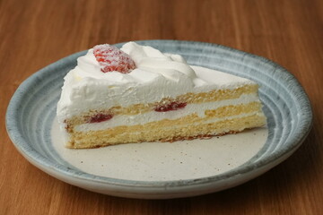 One small Japanese strawberry shortcake on a stylish Japanese plate on a wooden tray on a black cloth on a white table
