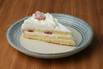 One small Japanese strawberry shortcake on a stylish Japanese plate on a wooden tray on a black cloth on a white table