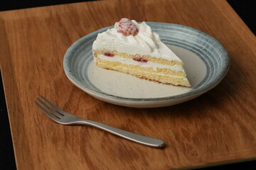 One small Japanese strawberry shortcake and a small fork on a stylish Japanese plate on a wooden tray on a black cloth on a white table
