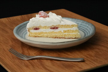 One small Japanese strawberry shortcake and a small fork on a stylish Japanese plate on a wooden tray on a black cloth on a white table