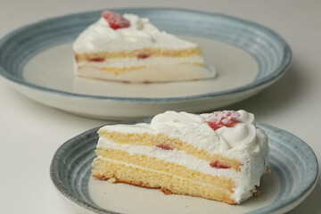 Two Japanese strawberry shortcakes, one on a stylish small plate and one on a large plate, on a white table
