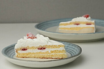 Two Japanese strawberry shortcakes, one on a stylish small plate and one on a large plate, on a white table