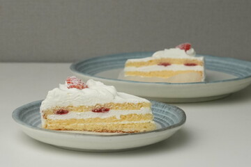 Two Japanese strawberry shortcakes, one on a stylish small plate and one on a large plate, on a white table