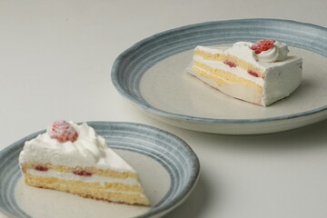 Two Japanese strawberry shortcakes, one on a stylish small plate and one on a large plate, on a white table