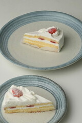 Two Japanese strawberry shortcakes, one on a stylish small plate and one on a large plate, on a white table
