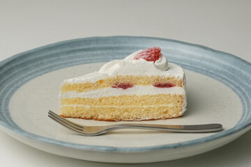 One small Japanese strawberry shortcake and a big fork on a stylish big plate on a white table