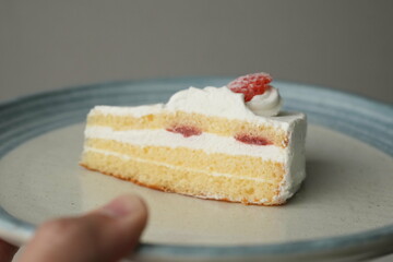 Japanese hand holding one small Japanese strawberry shortcake on a stylish big plate on a white table