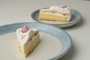 Two Japanese strawberry shortcakes, one on a stylish small plate and one on a large plate, on a white table