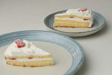 Two Japanese strawberry shortcakes, one on a stylish small plate and one on a large plate, on a white table