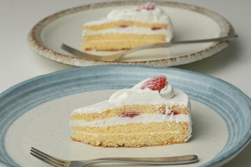Japanese strawberry shortcake and fork on each stylish large and small plate on a white table