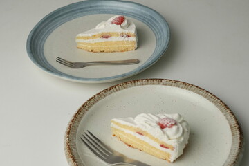 Japanese strawberry shortcake and fork on each stylish large and small plate on a white table
