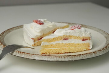 Two Japanese strawberry shortcakes and a large fork on a stylish large plate on a white table