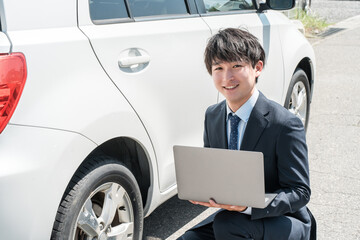 中古車を査定する営業マン・中古車査定士のスーツ姿の若いアジア人男性
