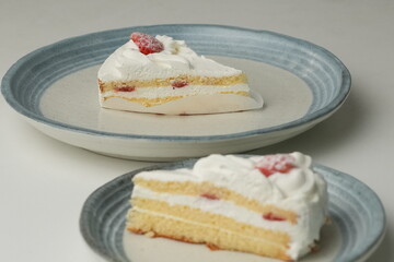 Two Japanese strawberry shortcakes, one on a stylish small plate and one on a large plate, on a white table