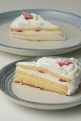 Two Japanese strawberry shortcakes, one on a stylish small plate and one on a large plate, on a white table