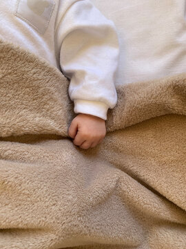 Hand of  newborn baby covered with  soft beige blanket.  Top view.  