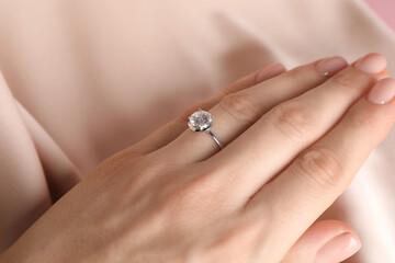 Woman wearing beautiful ring with gemstone against beige fabric, closeup